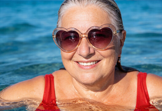 &auml;ltere Frau beim Schwimmen im Meer mit herzf&ouml;rmiger Sonnenbrille