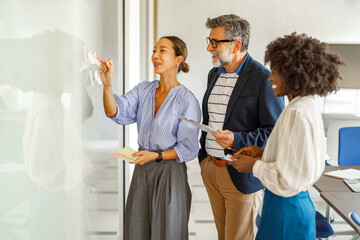 Confident businesswoman explaining innovative ideas to colleagues over sticky notes in office...