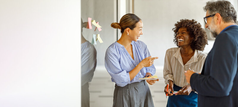 Cheerful colleagues brainstorming ideas using sticky notes during collaborative corporate strategy meeting