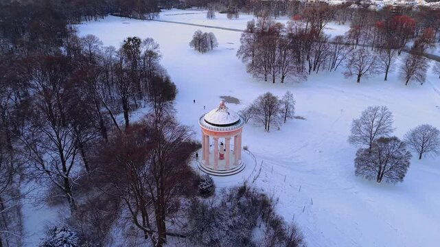 Sunrise at Monopteros with Munich city center view. Aerial shot of the snow-covered park and the distant silhouette of the Frauenkirche cathedral and City Hall during a sunny winter day. 