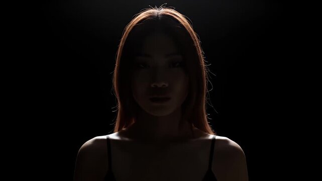 Potrait of a Young Woman in Black Tank Top Against Dark Background with Strong Lighting and Shadow Play Focus on Face