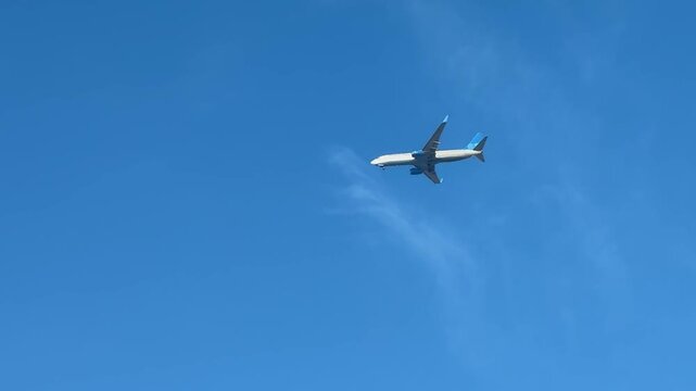 A generic white twin-engine narrow-body Boeing 737 commercial passenger airplane flying low over snow-covered trees against a clear blue sky.