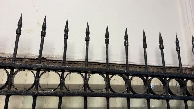 Old wrought iron fence with sharp spikes and decorative circles, set against a grunge wall. Captures a vintage, security aesthetic. Ideal for themes of history, architecture, and protection.