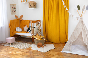 Child wigwam with cotton flags at home. Playroom with toys. Modern interior design of a child bedroom with teepee tent. Cozy yellow Scandinavian baby room: crib with bedding, pouf and carpet on floor © stock_studio