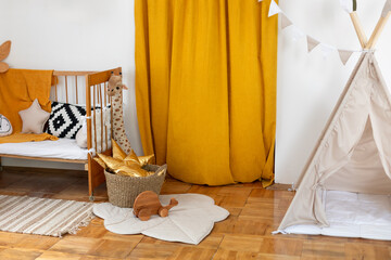 Child wigwam with cotton flags at home. Playroom with toys. Modern interior design of a child bedroom with teepee tent. Cozy yellow Scandinavian baby room: crib with bedding, pouf and carpet on floor © stock_studio