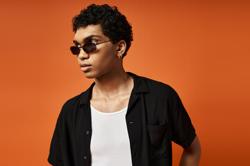Fototapeta premium Stylish young man with curly hair and sunglasses poses in vibrant studio backdrop