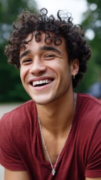 Portrait of a joyful young man with curly hair and glowing skin smiling at the camera outdoors in the park 