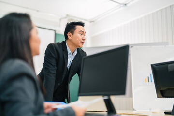 Naklejka premium Serious Asian businessman leans over a boardroom table, presenting and discussing strategy with colleagues, communication, teamwork, leadership, and positive corporate engagement