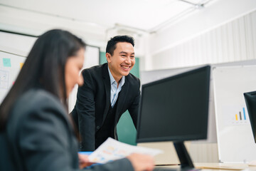 Naklejka premium Laughing Asian businessman leans over a boardroom table, leading a discussion and presentation with colleagues, communication, teamwork, leadership, and positive corporate culture