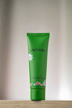 STRASBOURG, FRANCE - JANUARY 15, 2026 : A still life photographe of Marc Jacobs Daisy Wild body lotion tube packaging. The product is displayed on a wooden surface, cream drapes background in soft