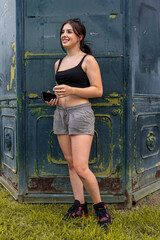 Young woman smiling holding a mobile phone outdoors in casual crop top and shorts