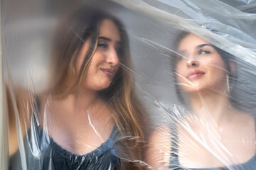 Women posing behind clear plastic wrap creating an artistic, blurred, and abstract effect