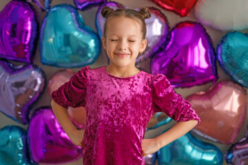 Happy child girl in pink dress posing with heart-shaped balloons on Valentine’s Day. Festive...