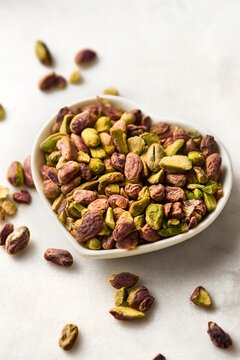 Pistachio nuts without shell in a heart shaped bowl on a white marble background. High angle view