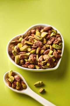 Pistachio nuts without shell in a heart shaped bowl on a green background. Spoon with pistachios. Green color.  High angle view