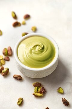 Pistachio cream spread in a white bowl on a white marble background. High angle view
