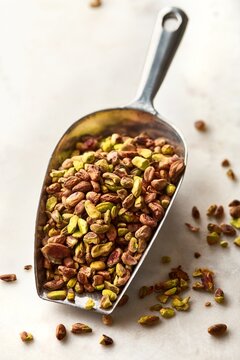 Pistachio nuts without shell in a steel scoop on a white marble background. High angle view