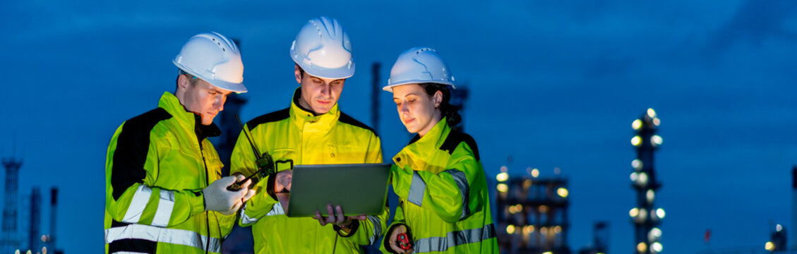 Petrochemical industry night engineer teamwork working on laptop Team of Petroleum in Glowing Workwear Collaborating oil refinery plant construction site at night