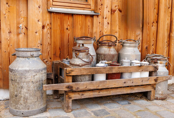 Collection of vintage metal milk cans and pails in a wooden rack against a rustic barn wall &ndash; traditional dairy farming, rural nostalgia and country life concept in alpine style