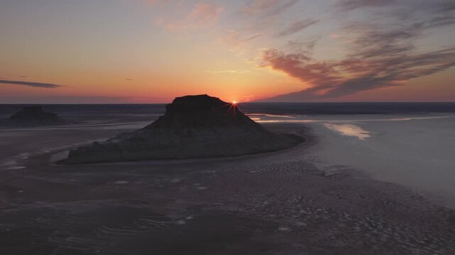 Aerial view of sunlight cresting the horizon, illuminating the stark rock formations in the landscape, Karynzharyk, Mangystau Region, Kazakhstan.