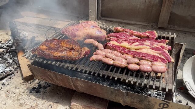 Variety of Argentine meat cuts including tira de asado, chorizo, and vacio grilling on a handmade metal rack. Authentic construction site barbecue tradition with heavy smoke