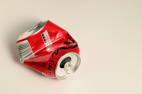 A crushed can of Coca-Cola sits on a white surface