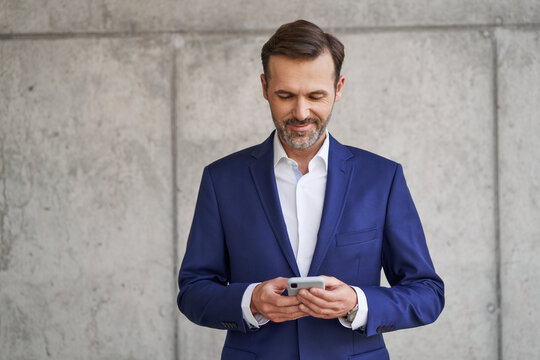 Mid adult businessman using mobile phone standing against concrete wall