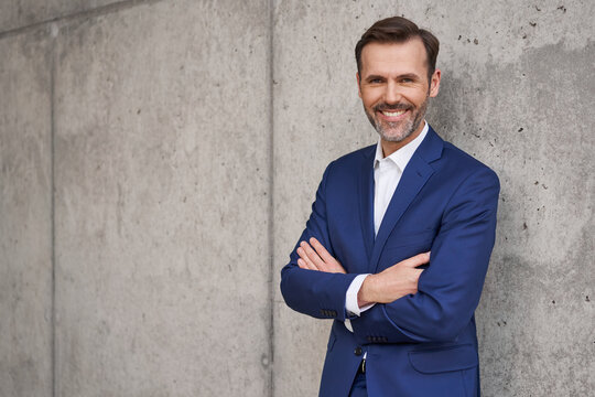 Portrait of smiling businessman standing against concrete wall, copy space