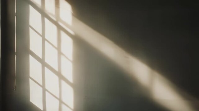 Sunlight streams through a window, casting graphic diagonal and grid patterned shadows onto a white interior wall, creating an abstract background texture
