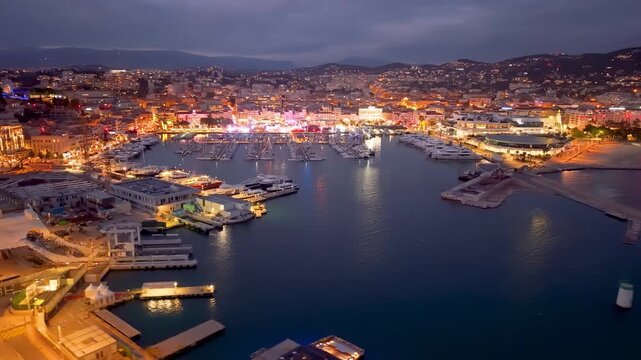 Aerial Footage Showcases Vibrant Waterfront Illumination Against City And Mountain Skyline Backdrop. Cannes. France