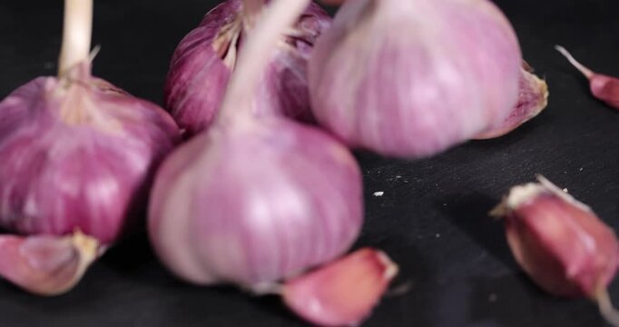 ripe purple garlic scattered on a black table in the kitchen and cloves of crushed garlic , garlic spices lie on a slate board in the kitchen over cooking