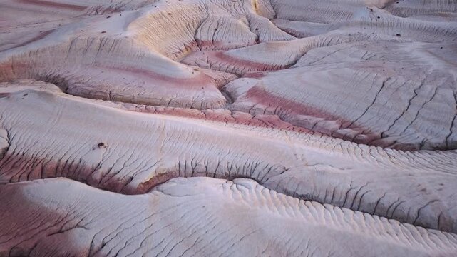 Aerial view of a desolate landscape revealing the stark beauty of arid terrain, accented by red striations cutting through the pale earth, Karynzharyk, Kazakhstan.