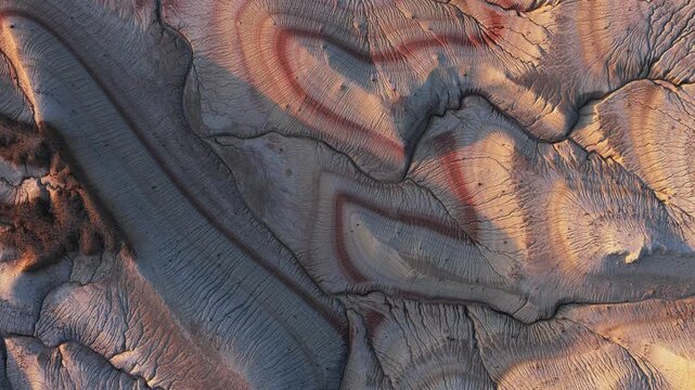 Aerial view of a textured landscape with earthy tones and striped patterns carved into the terrain, Karynzharyk, Mangystau Region, Kazakhstan.