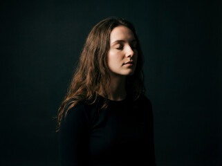 Naklejka premium Serene young woman with closed eyes on black background