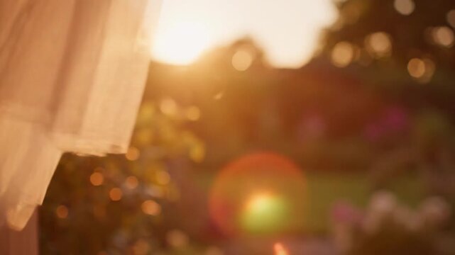 Beautiful white tulle curtains blowing in wind open window during a golden sunset, creating a peaceful and romantic atmosphere with warm sunlight and soft garden bokeh