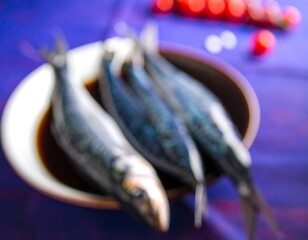 A slightly blurred, close-up shot showcases fresh, silvery fish arranged in a shallow, round bowl. Background features cherry tomatoes