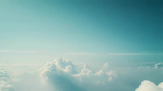 Fluffy white clouds fill the lower part of the frame, resting peacefully under a wide open light blue sky, creating a serene and vast aerial background view