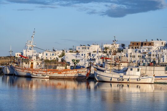View of Naoussa, Fishing boats in the harbour at sunset, reflected in the sea, White Cycladic houses, Naoussa, Paros, Cyclades, Greece