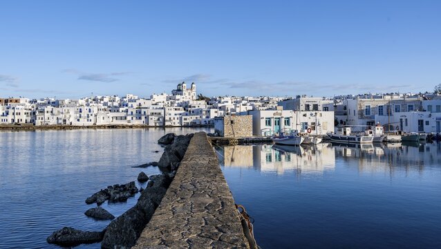 Harbour wall, local view of Naoussa town and blue sea, harbour with fishing boats and reflection, white Cycladic houses and church Agios Faneromeni, Paros, Cyclades, Greece