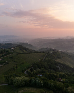 Aerial view of rolling hills and vineyards basked in the soft glow of the setting sun, creating a serene and picturesque landscape, Alba, Italy.