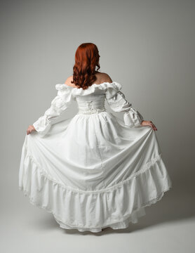 full length portrait redhead female model wearing historical fantasy wedding dress, fairytale ball gown.  posing walking away from camera, isolated figure on white studio background