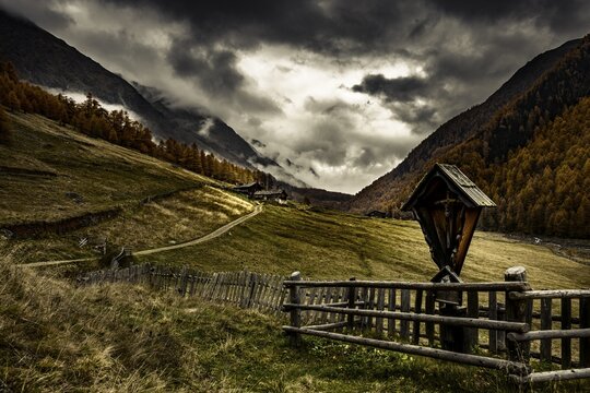 Way cross with alpine hut in autumnal mountain landscape with threatening cloudy sky, Pfossental, Merano, Vinschgau, South Tyrol, Italy