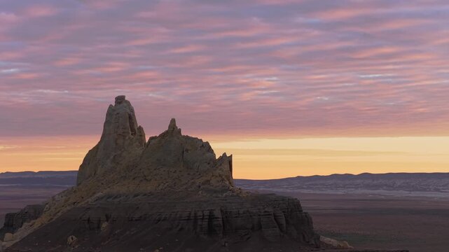 Aerial view of a striking rock formation silhouetted against a vibrant sunset, with pink and orange hues painting the sky, Shetpe, Mangystau Region, Kazakhstan.