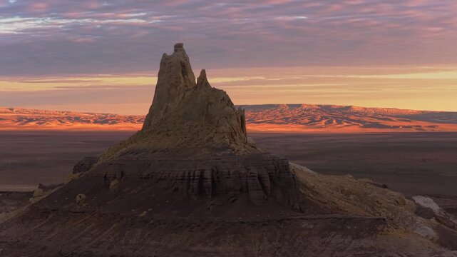 Aerial view of a dramatic rock formation silhouetted against a vibrant sunset, casting long shadows across the arid landscape, Shetpe, Mangystau Region, Kazakhstan.
