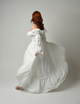 full length portrait redhead female model wearing historical fantasy wedding dress, fairytale ball gown.  posing walking away from camera, isolated figure on white studio background