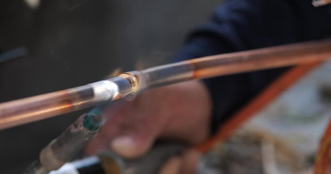 A technician or worker is soldering copper pipes; an air conditioning technician.
