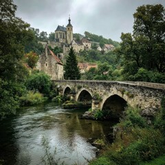Obraz premium A picturesque medieval village with a stone bridge spanning a river, surrounded by lush greenery and ancient stone buildings, under a cloudy sky with a church steeple in the background.