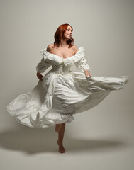 full length portrait redhead female model wearing historical fantasy wedding dress, fairytale ball gown.  isolated figure dancing with flowing fabric on white studio background