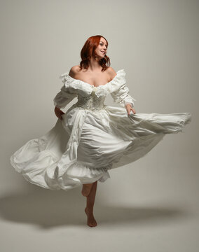 full length portrait redhead female model wearing historical fantasy wedding dress, fairytale ball gown.  isolated figure dancing with flowing fabric on white studio background