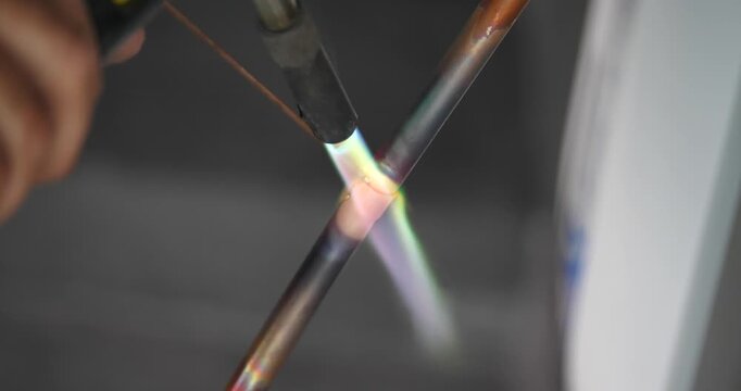A technician or worker is soldering copper pipes; an air conditioning technician.